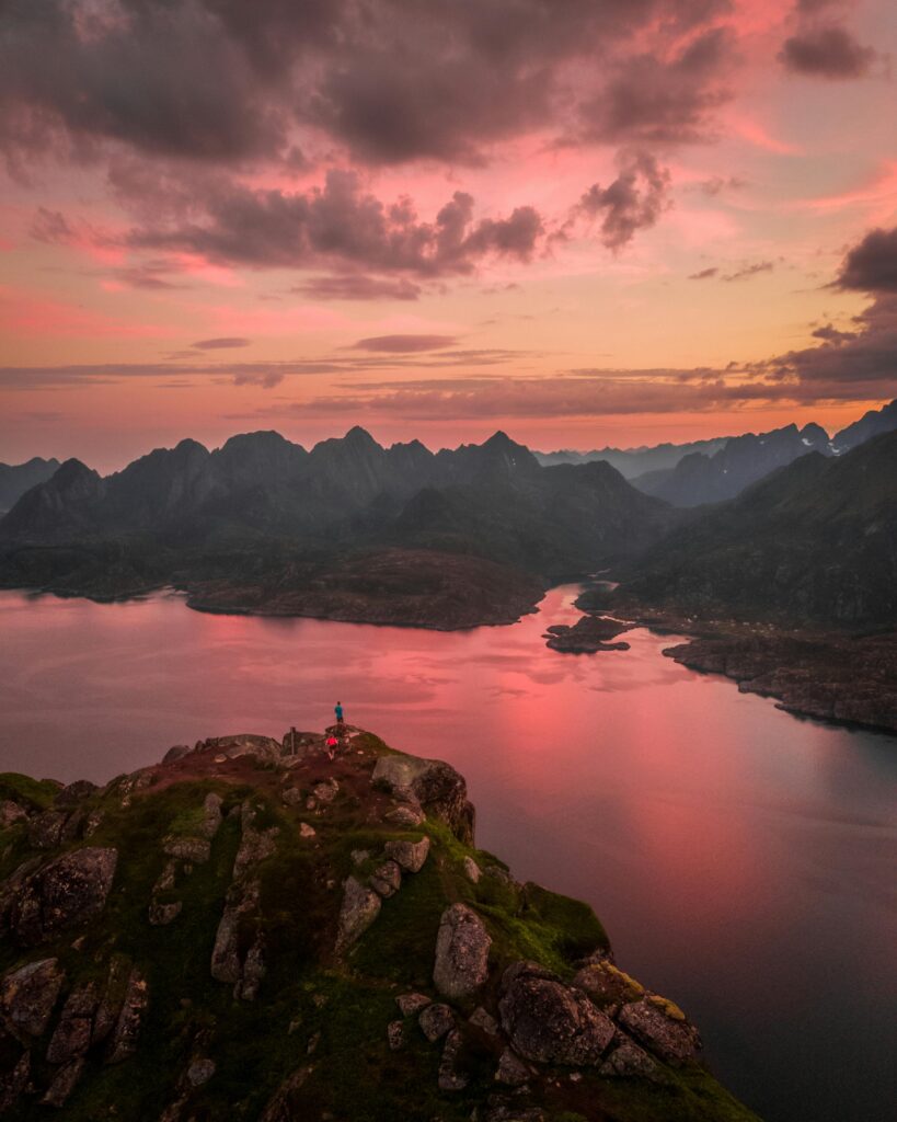 Breathtaking aerial shot of the Lofoten mountains in Norway with a vibrant sunset reflecting over the fjord.