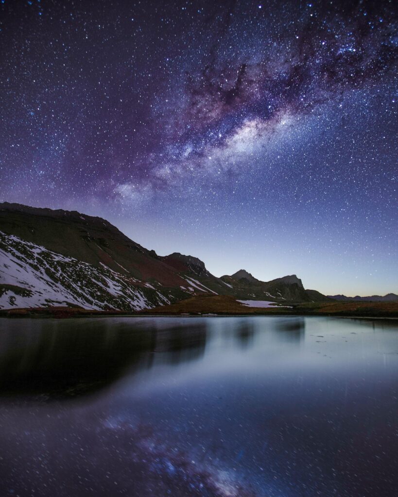 Breathtaking view of the Milky Way galaxy reflecting over a tranquil mountain lake at night.