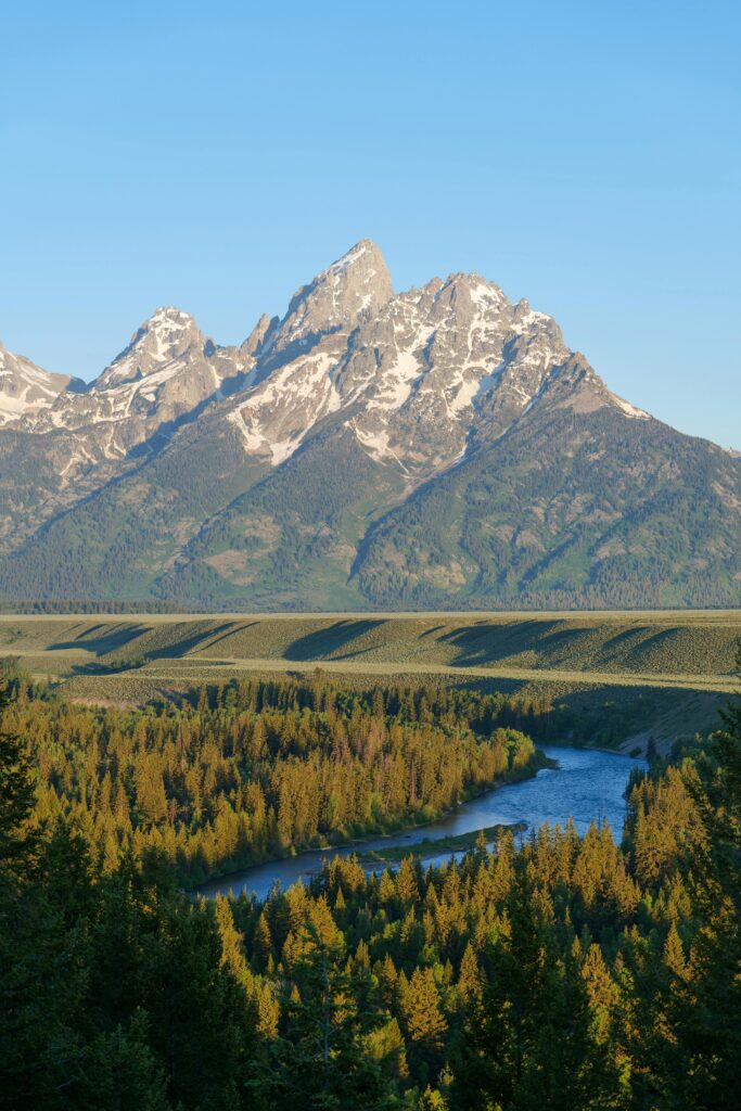 Breathtaking landscape of the Grand Teton mountains with lush forest and winding river, captured in Wyoming.
