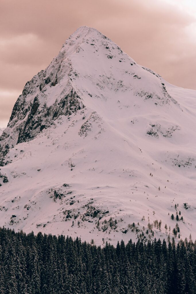 Enchanting snow-covered mountain peak surrounded by serene winter landscape with dense pine forest.